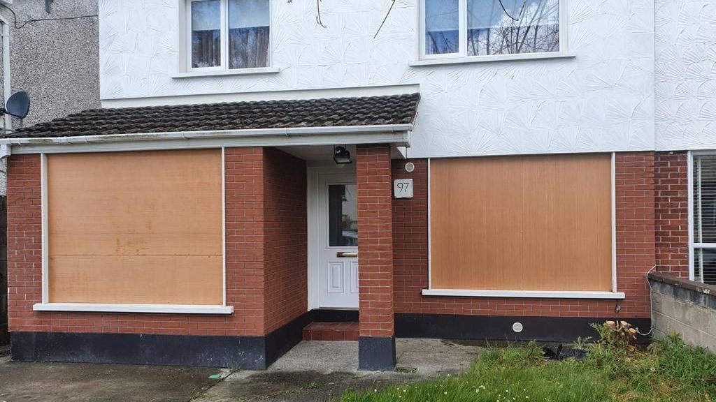 The front of a house with a brick wall and wooden windows.