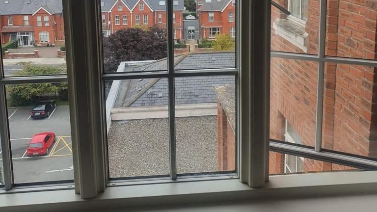 A window with a view of a brick building and a parking lot.