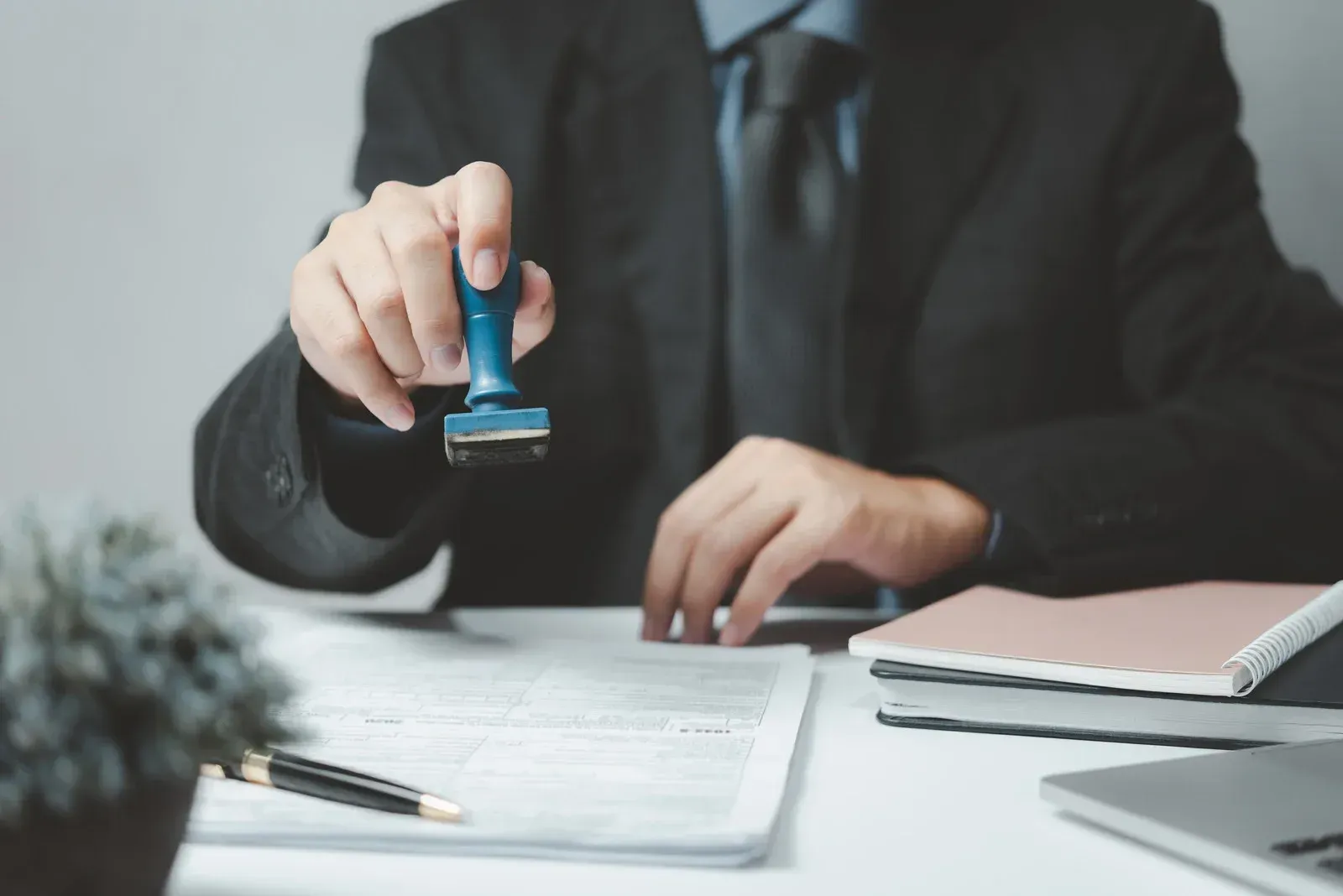 Person in suit stamps a document with a blue stamp at a desk.