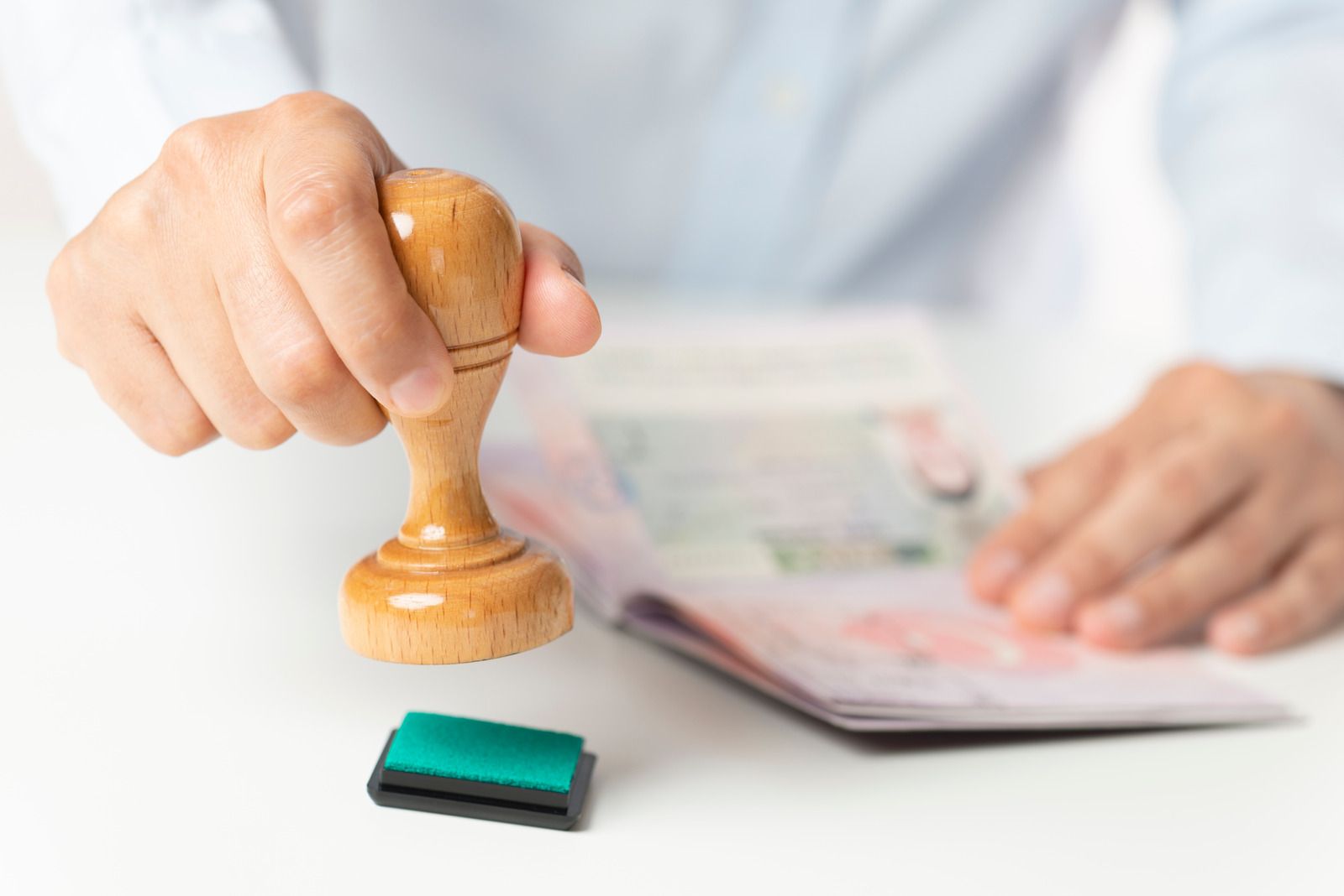 Hand stamping passport with wooden stamp and green ink pad.
