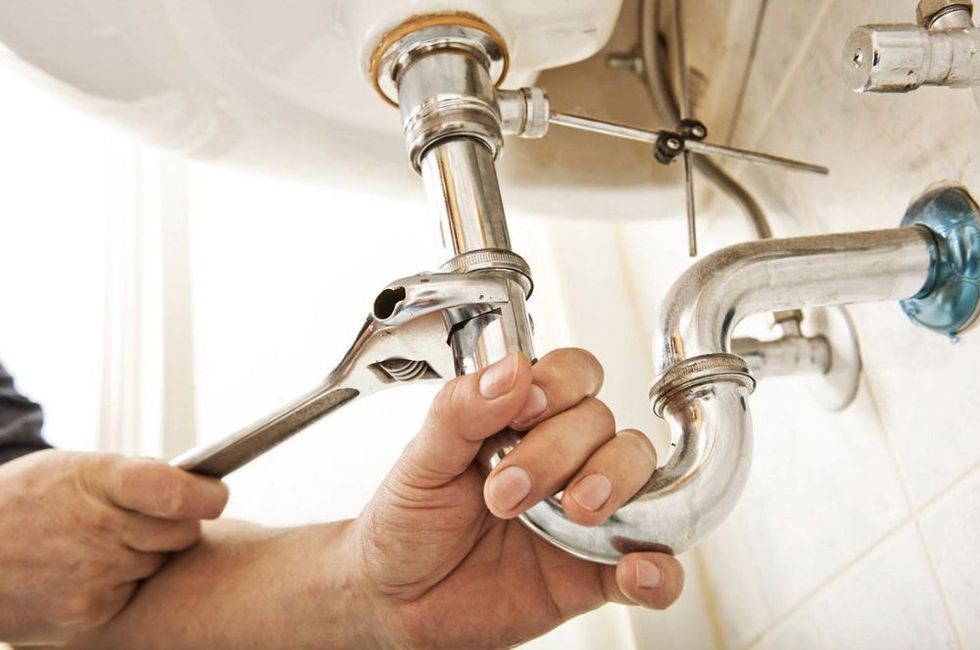 Close-up of hands using a wrench to repair chrome bathroom sink pipes under the basin.