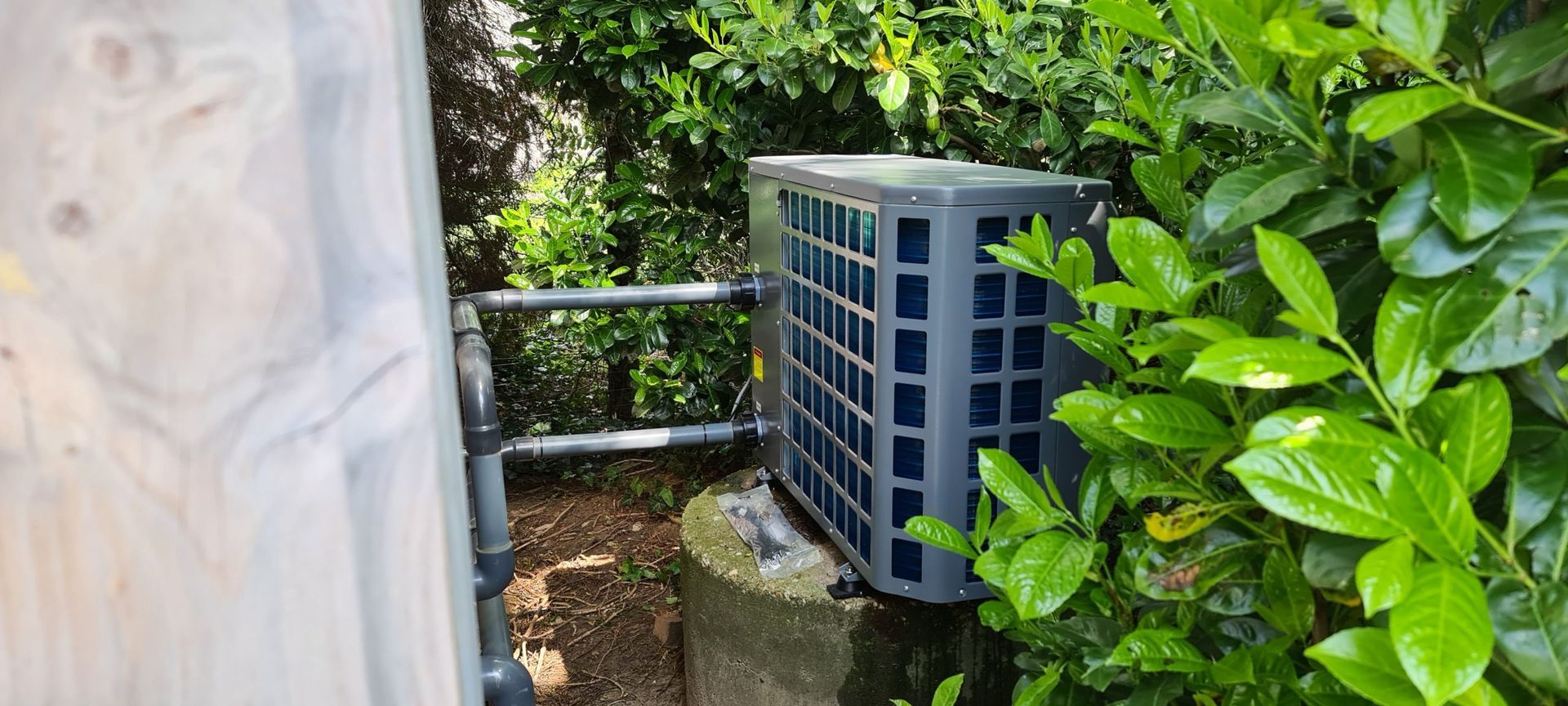 Een zwarte airconditioner staat naast een struik.