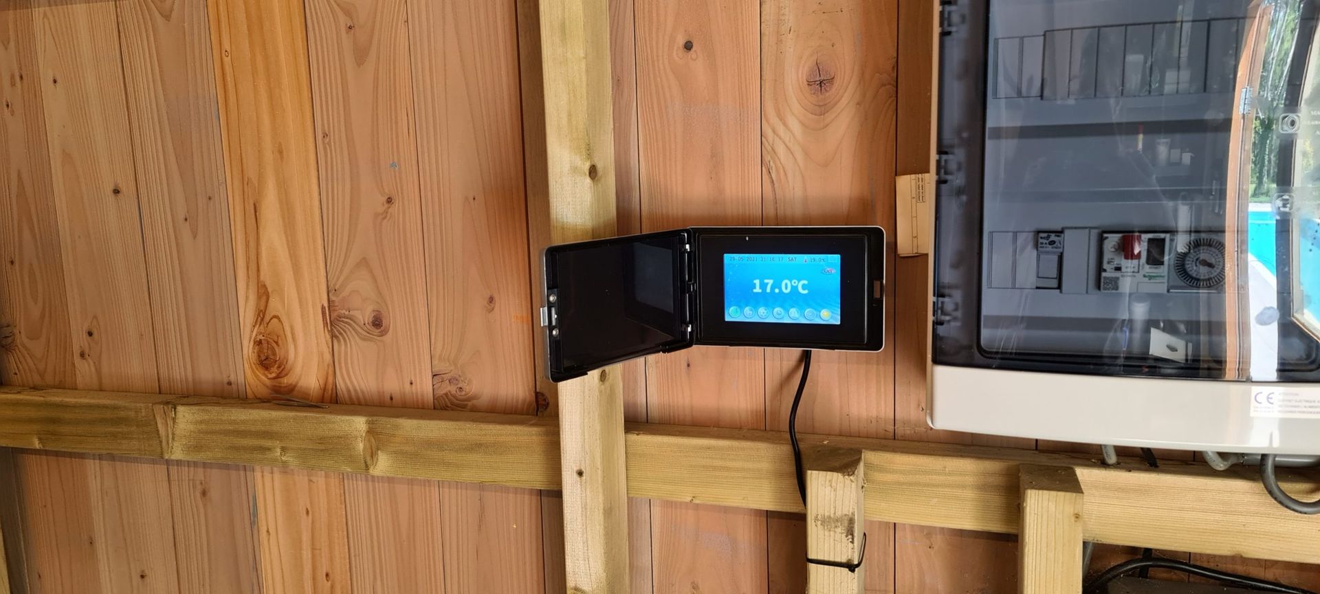 Een thermostaat hangt aan een houten muur naast een computermonitor.