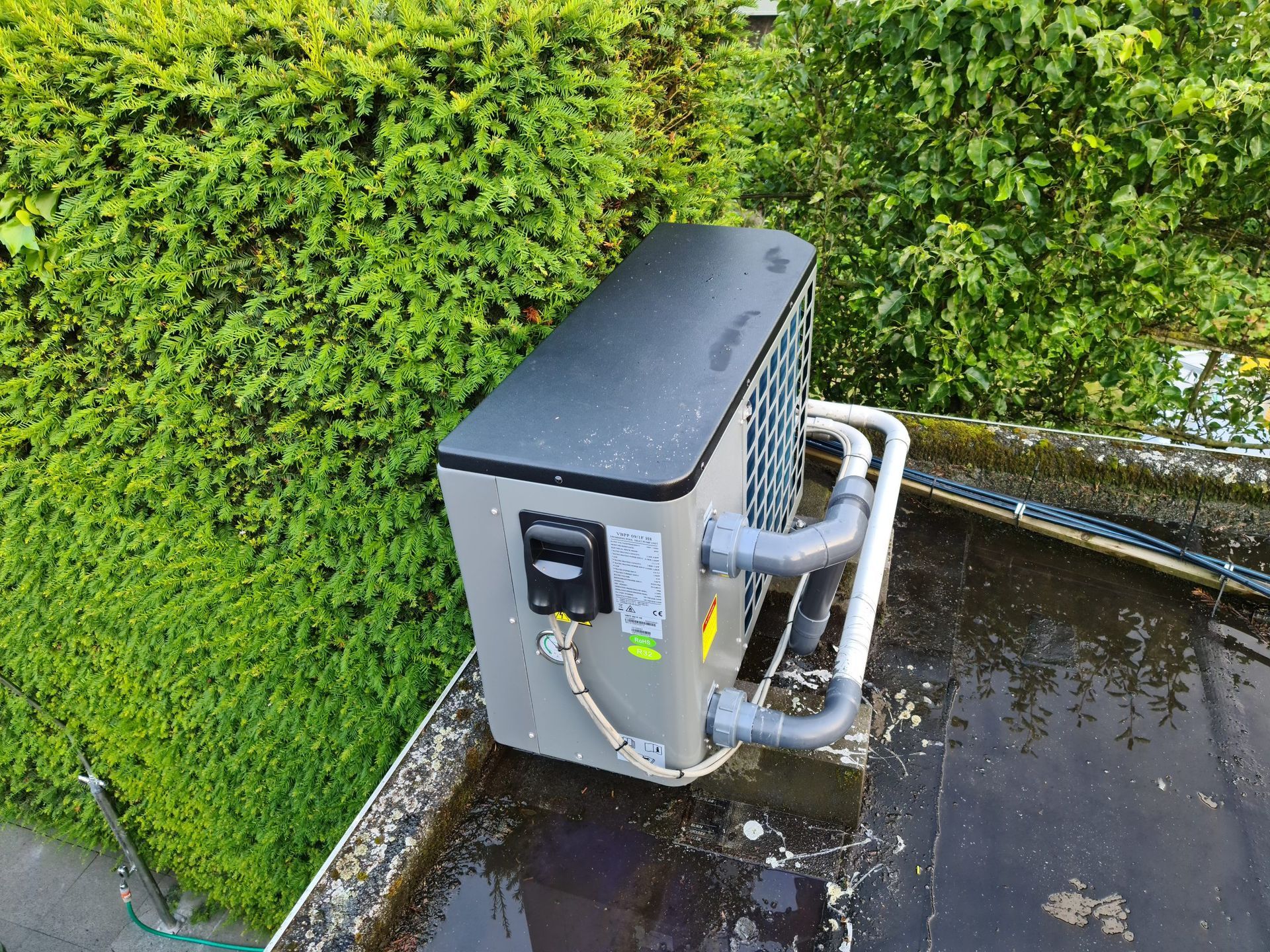 Een airconditioner staat op een dak naast een struik.