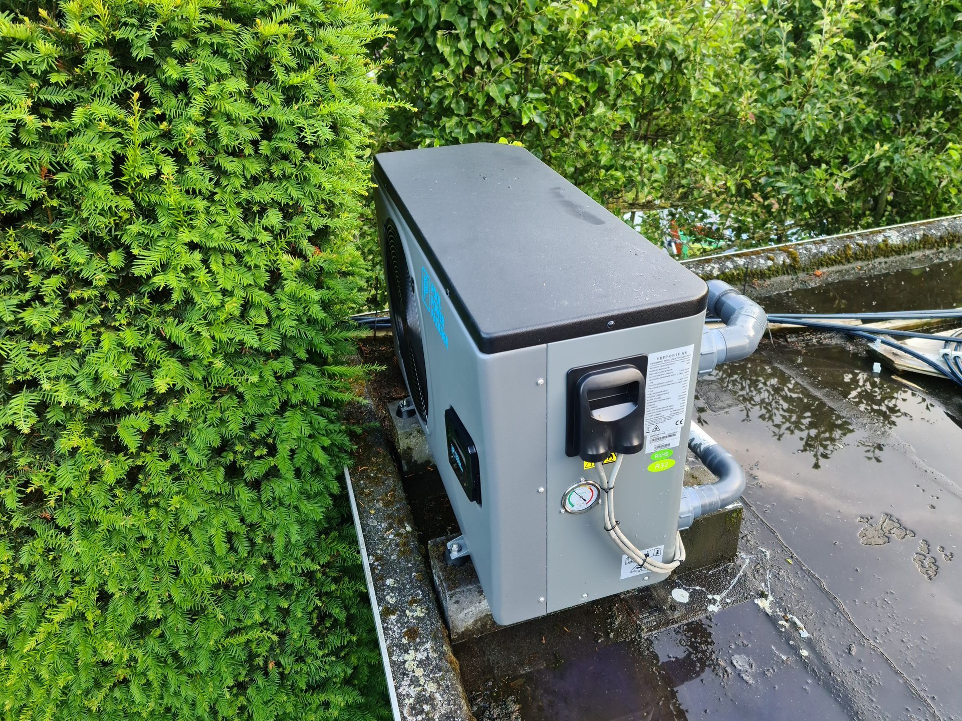 Een grote grijze doos staat op een dak naast een struik.