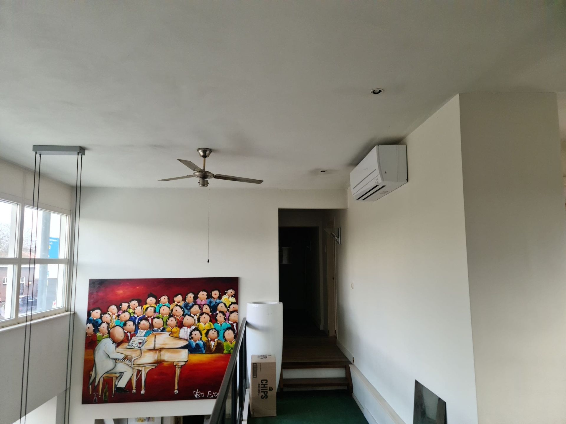 Een kamer met een schilderij aan de muur en een plafondventilator