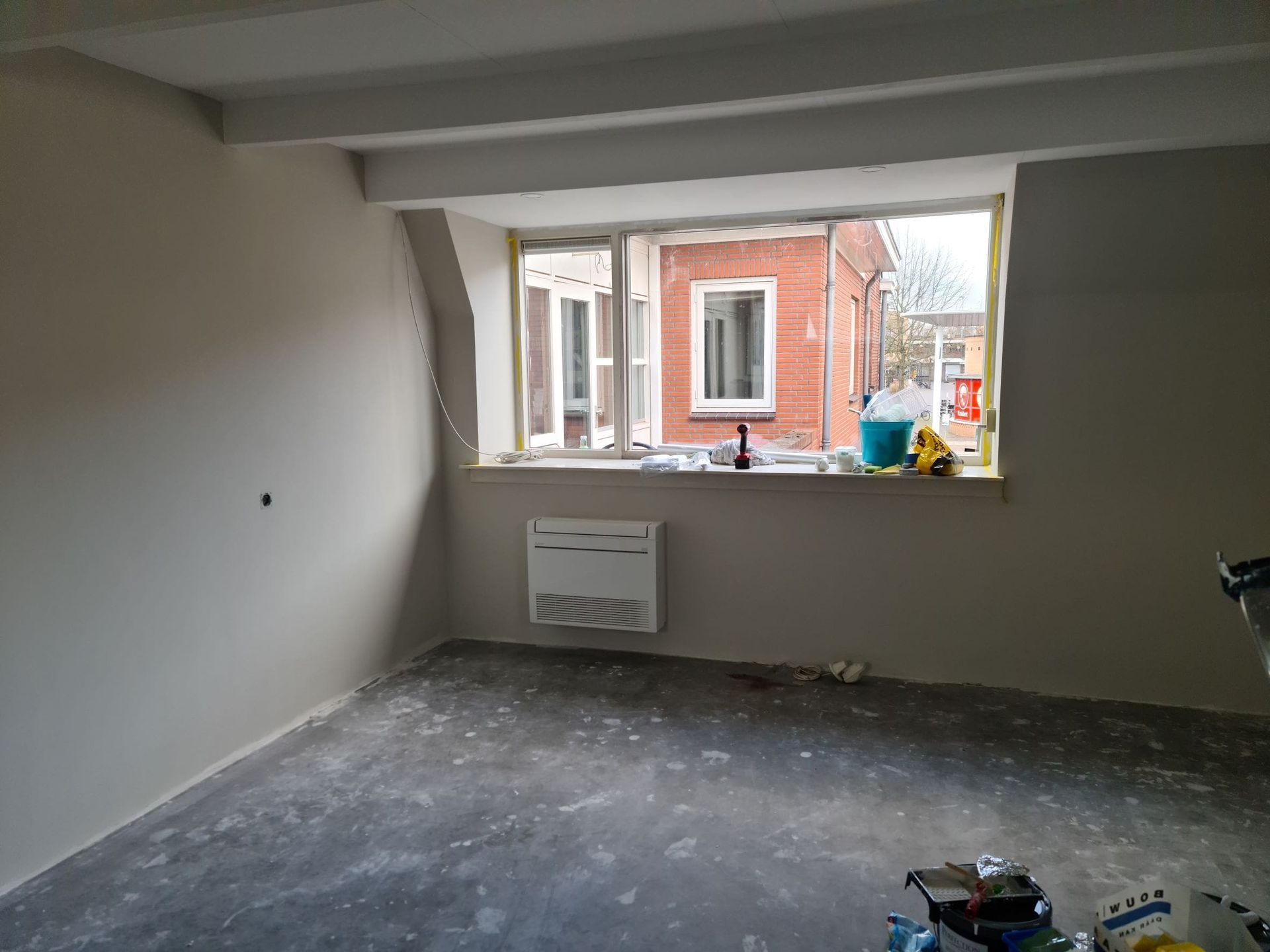 Een lege kamer met daarin een raam en een radiator.