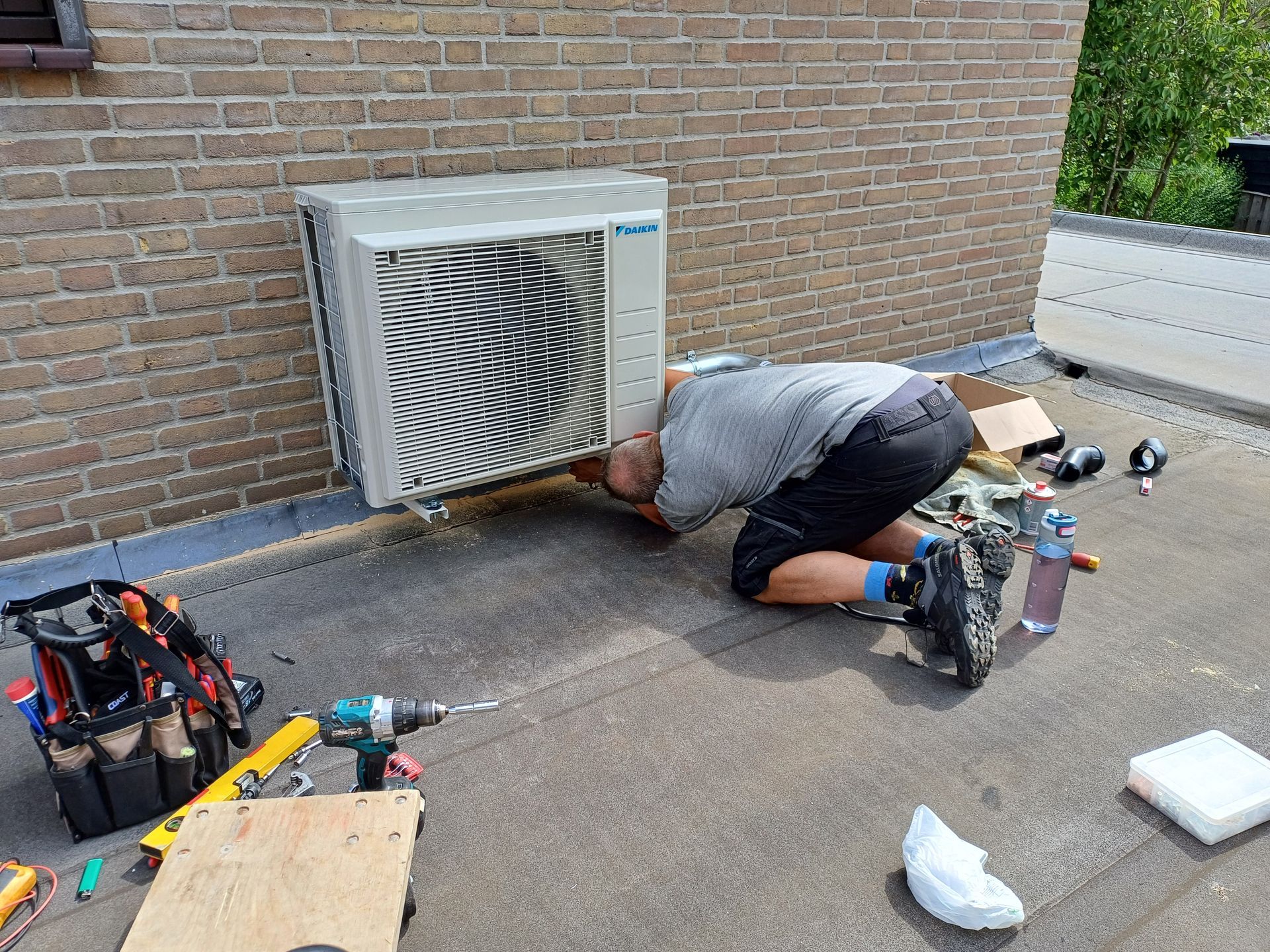 Professioneel onderhoud aan een Daikin airco voor optimale werking en langere levensduur. Monteur voert service en onderhoud uit aan een Daikin airconditioning buitenunit op een plat dak, omringd door gereedschap en onderdelen.