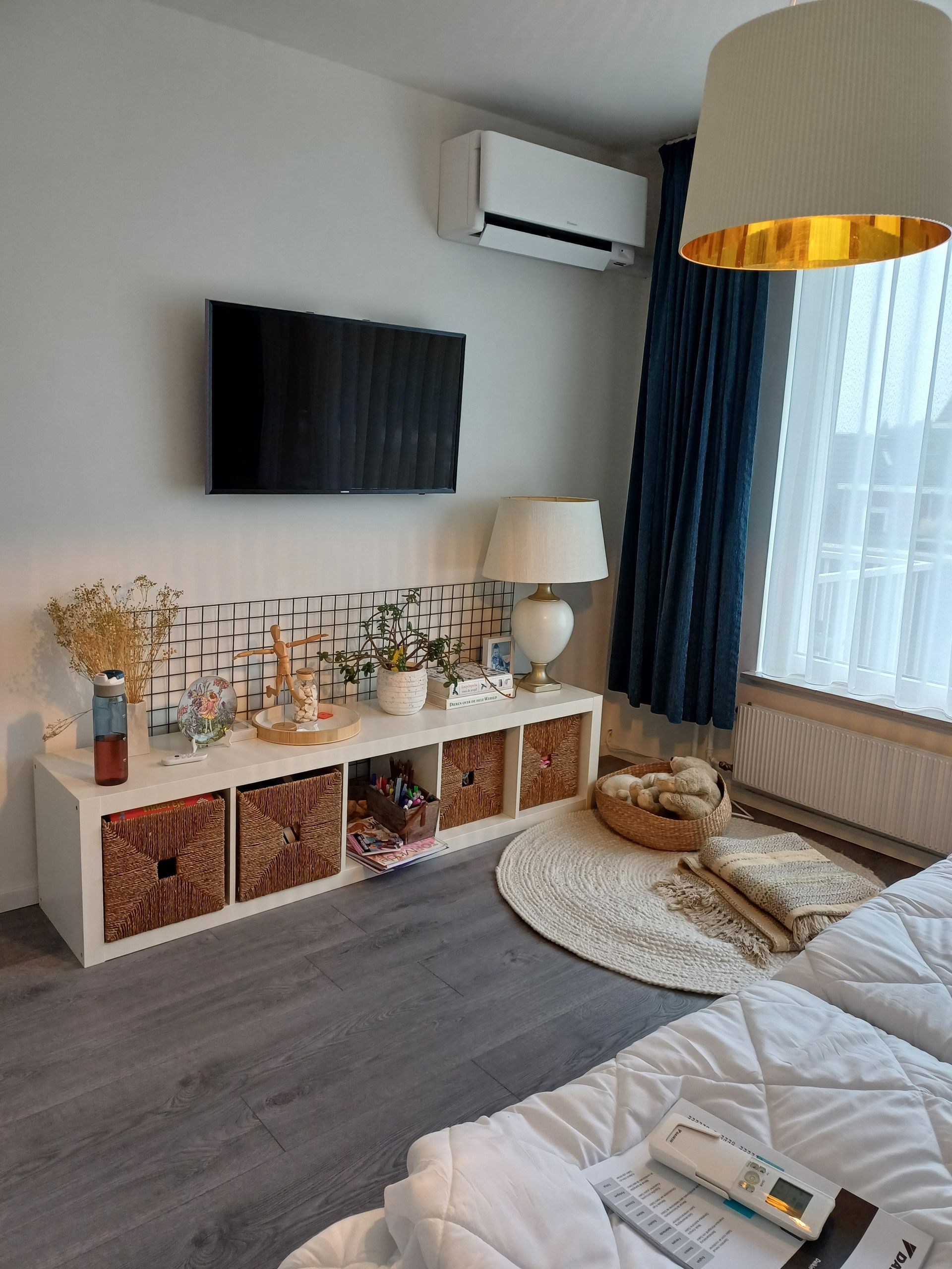 Wandgemonteerde Daikin Stylish airco in een modern ingerichte woonkamer, geplaatst boven een flatscreen-tv en naast een groot raam met donkere gordijnen.