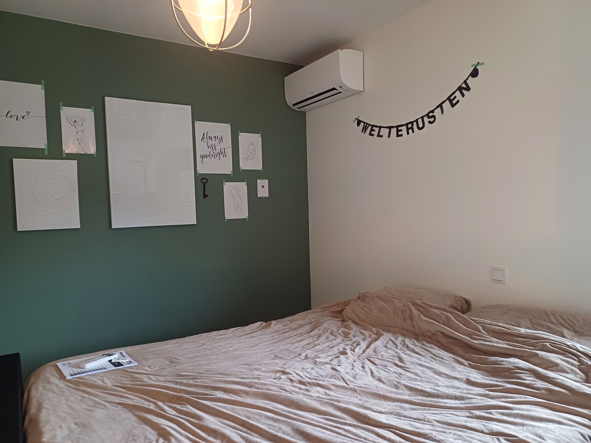 Slaapkamer met een opgemaakt tweepersoonsbed, groene en witte muren, minimalistische wanddecoratie en een witte Daikin airco multi-split unit gemonteerd aan de witte muur boven het bed.