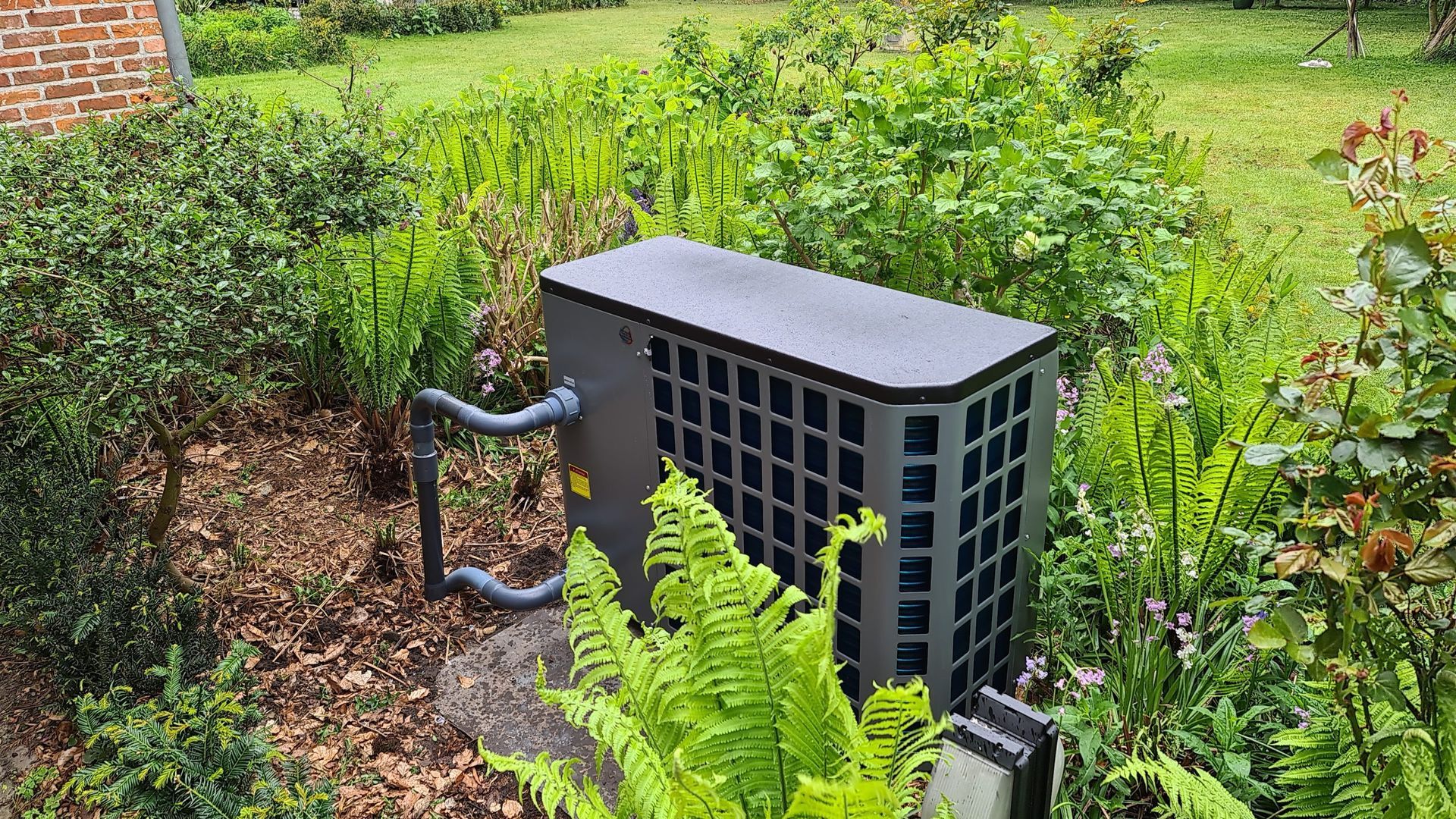 Een zwarte airconditioner staat midden in een weelderige groene tuin.