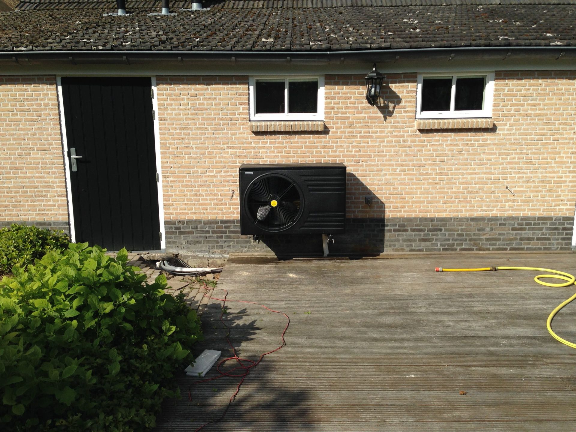 Een bakstenen gebouw met een zwarte deur en een zwarte ventilator aan de zijkant