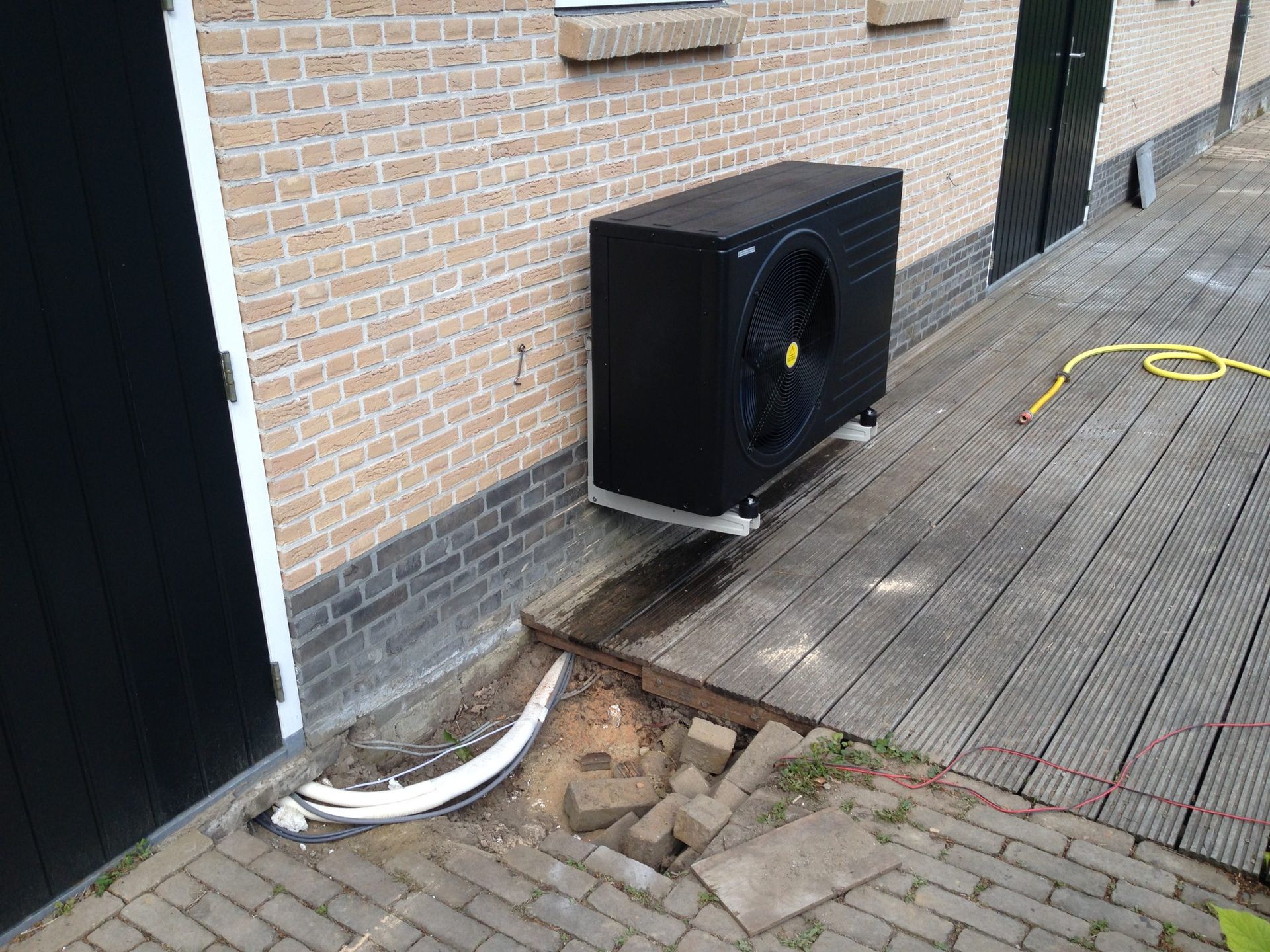 Een zwarte airconditioner staat op de zijkant van een bakstenen gebouw.