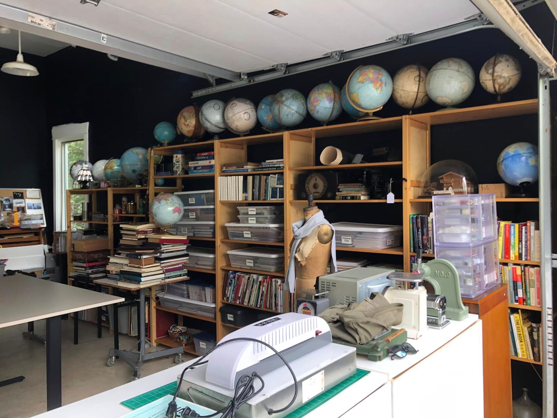 A workspace/studio with globes on shelves, books, storage bins, a desk, and equipment.