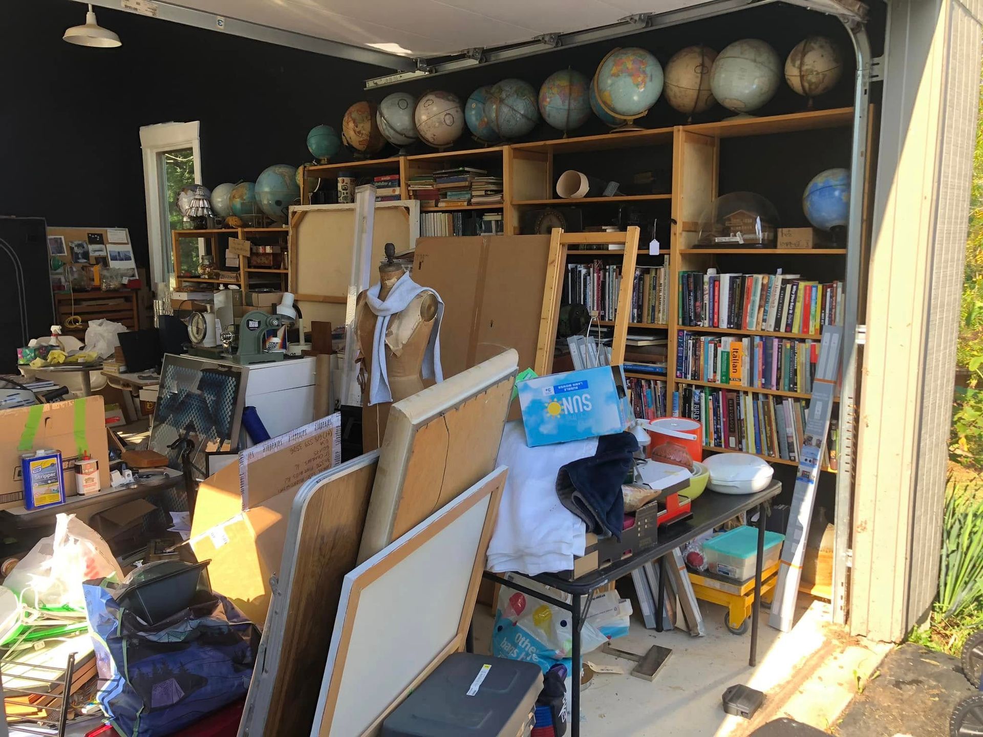 Cluttered studio with globes on shelves, easels, books, and art supplies; garage setting.