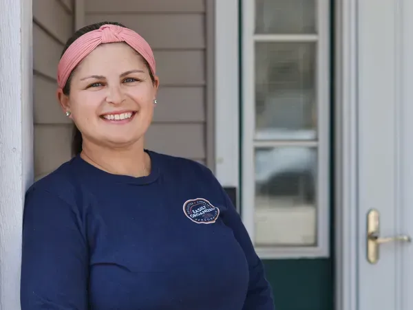 Woman in blue shirt and pink headband smiles near a doorway.
