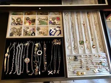 Open jewelry drawer with necklaces, bracelets, earrings, and other jewelry arranged in trays.