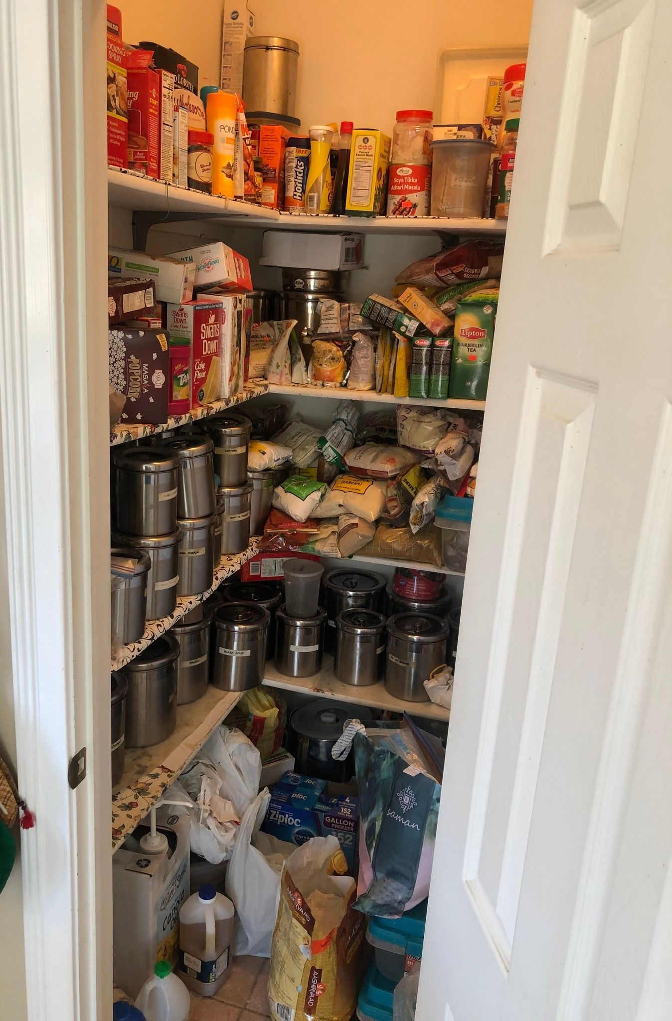 Cluttered pantry interior with shelves overflowing with food items and containers.
