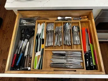 Wooden kitchen drawer with utensils: silverware, knives, scissors, and serving tools, neatly organized.