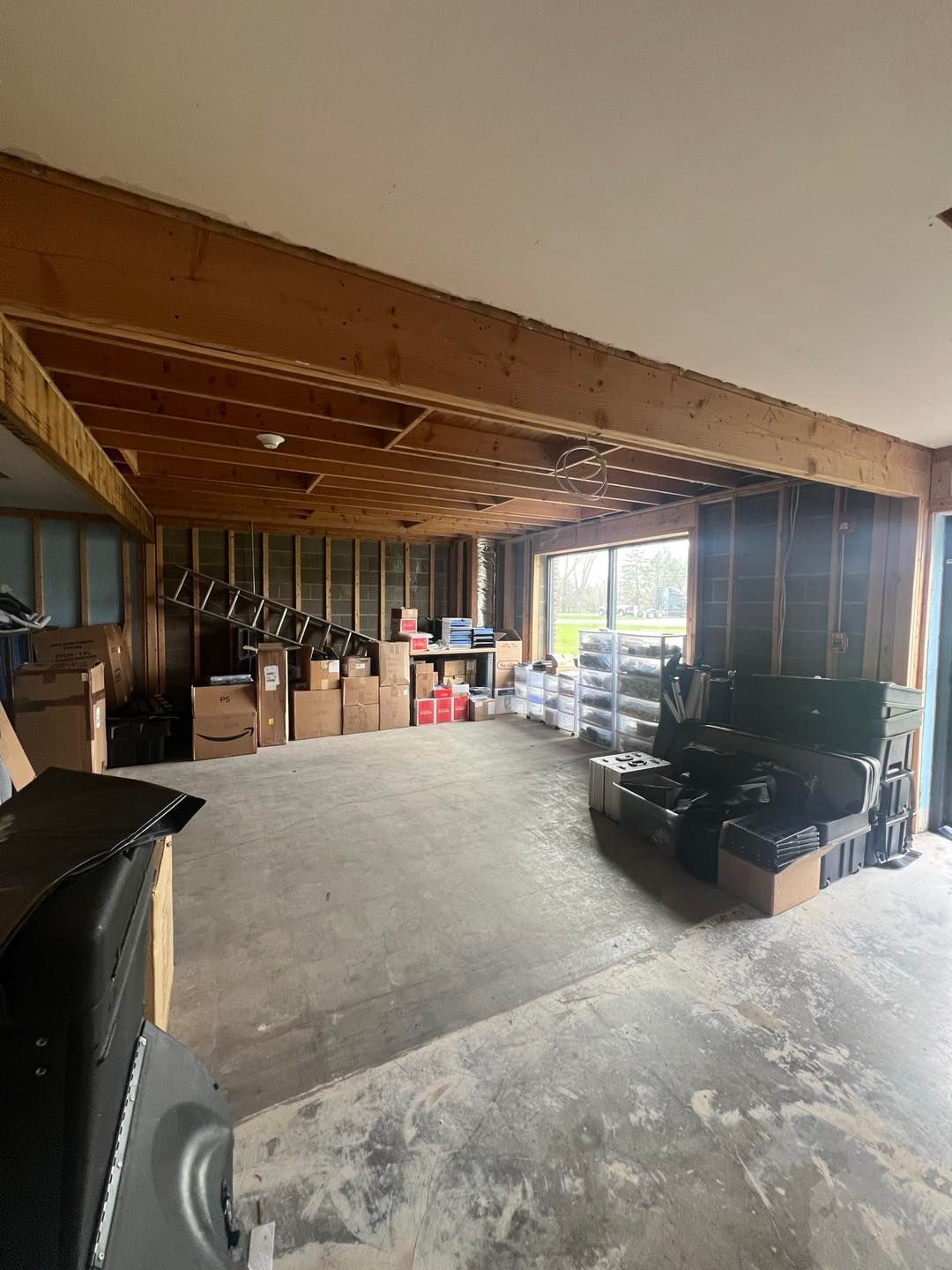 Unfinished room with exposed beams and studs; boxes and equipment scattered about; concrete floor.