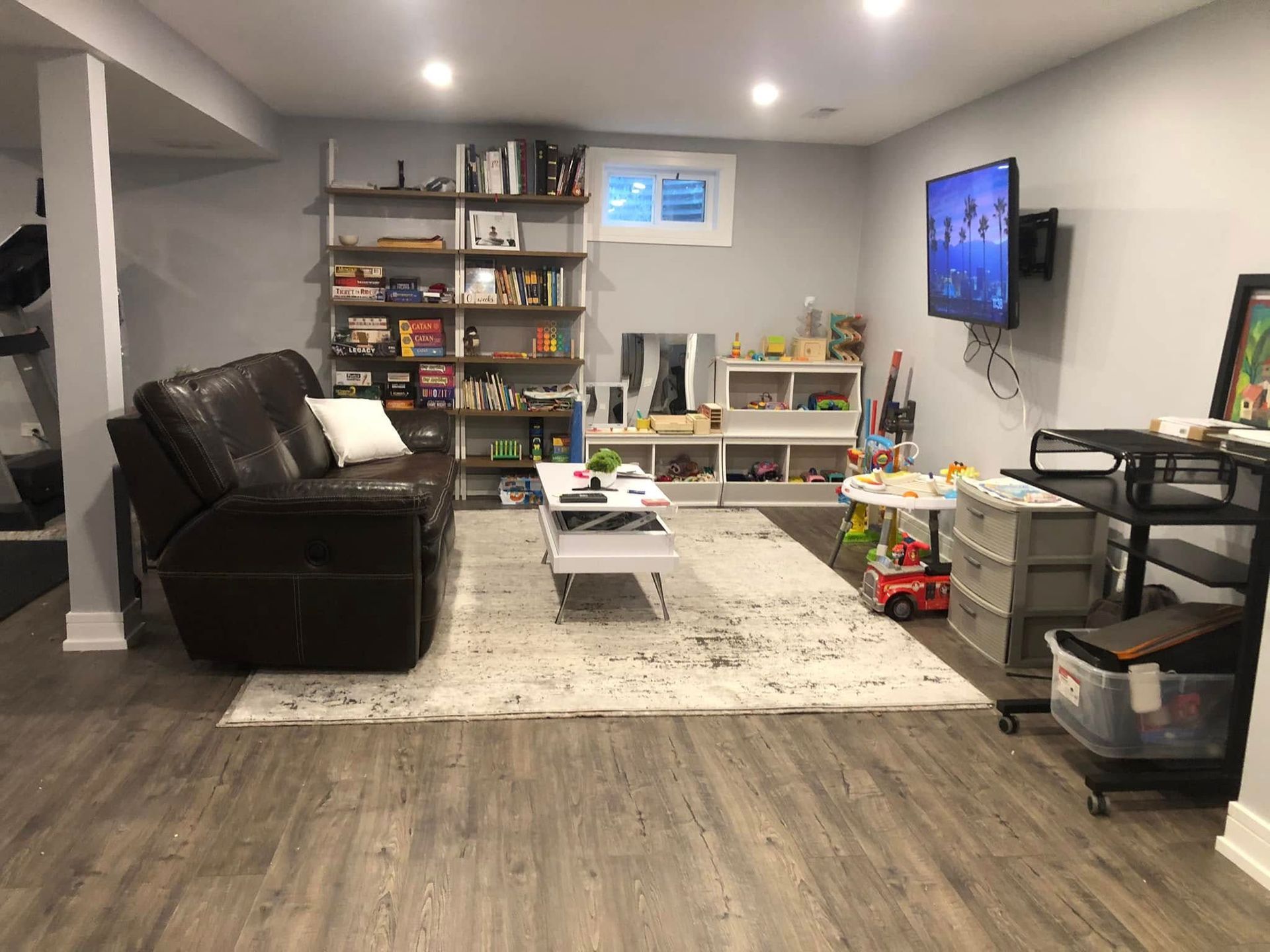 Living room with a dark recliner, TV, and shelves with books and toys.