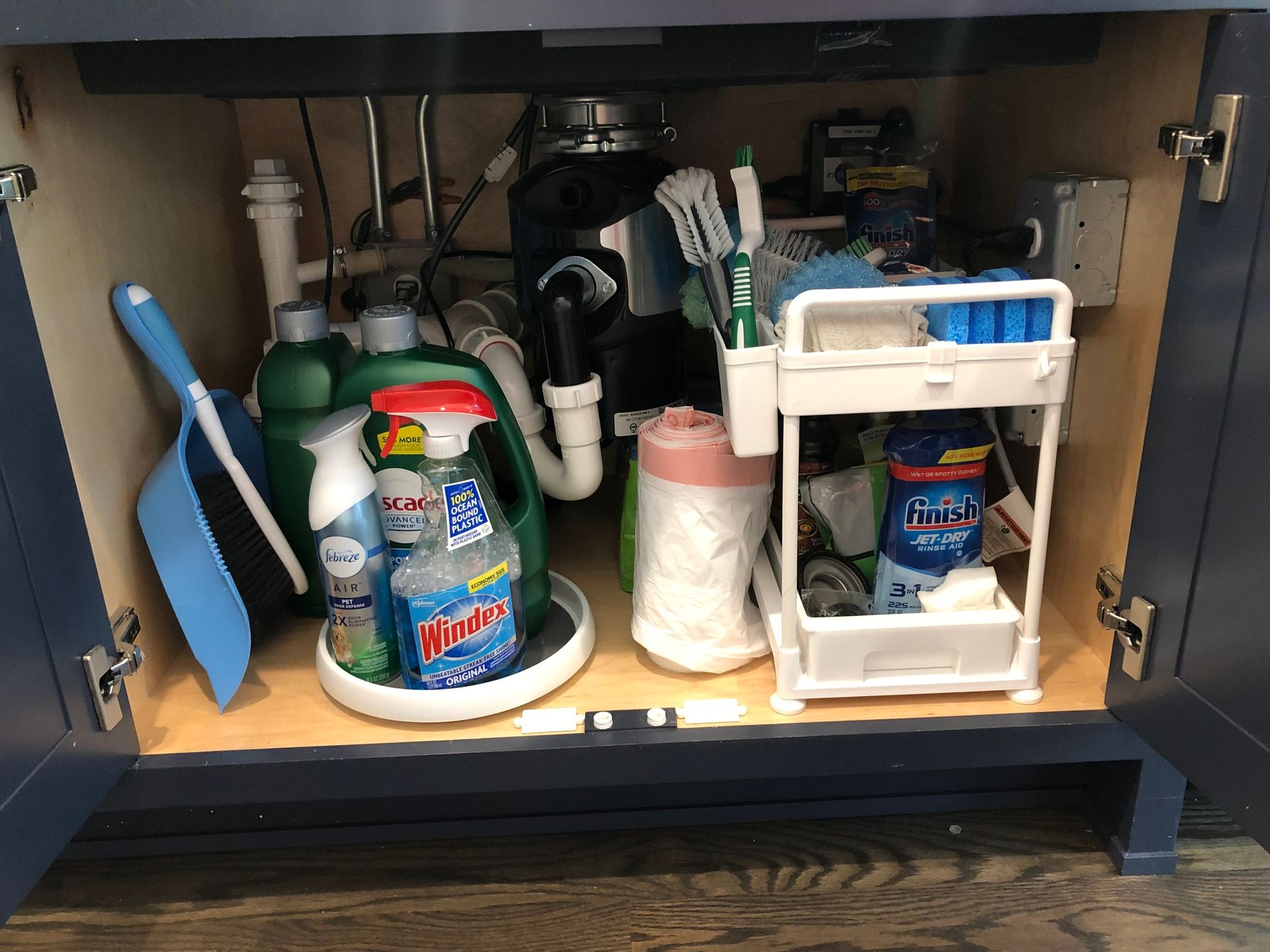 A partially open blue cabinet under a sink with cleaning supplies and a small white rolling storage cart.