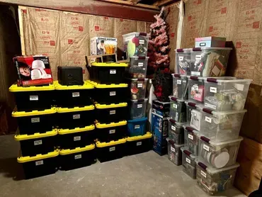 Storage containers in a basement, stacked against walls. Some black and yellow, others clear. Insulation in the background.