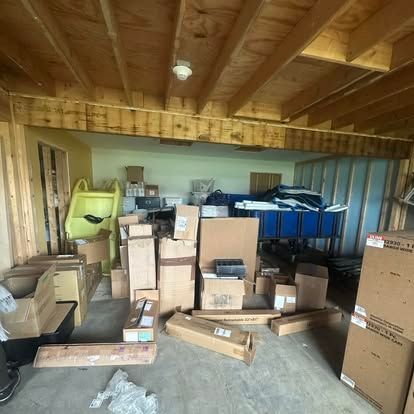 Storage room filled with cardboard boxes, wood beams overhead, blue bins in the back, and unfinished walls.