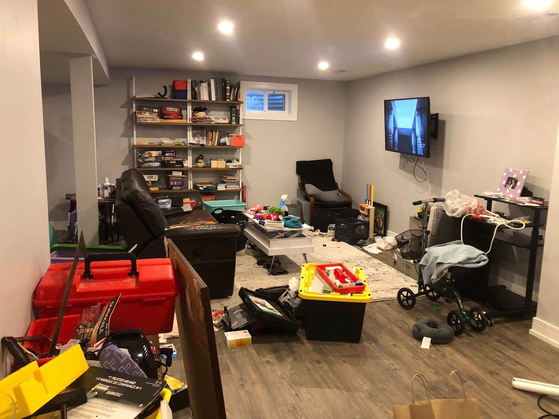 Cluttered basement room with a TV, shelves, and various items scattered on the floor.