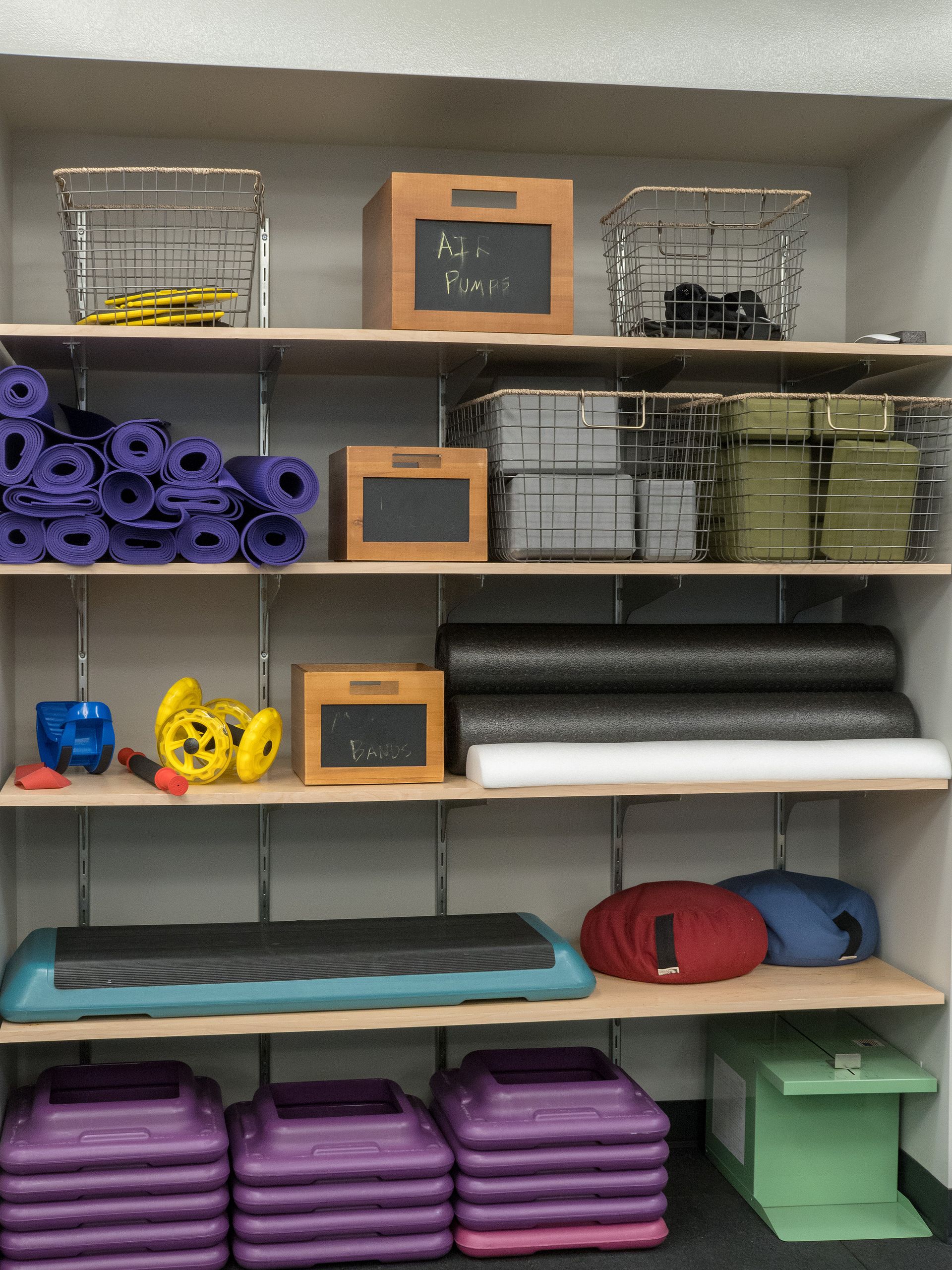Shelves in a fitness room stocked with exercise equipment, including mats, steps, and weights.
