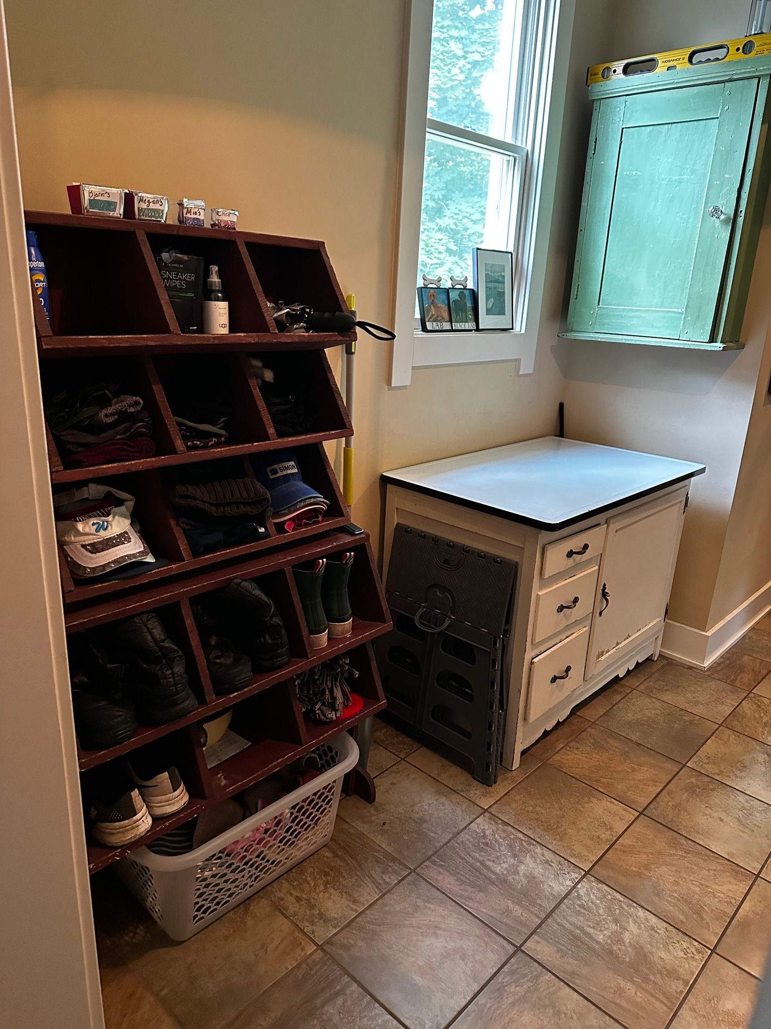 Shoe rack next to a small white cabinet by a window. The floor is tiled.