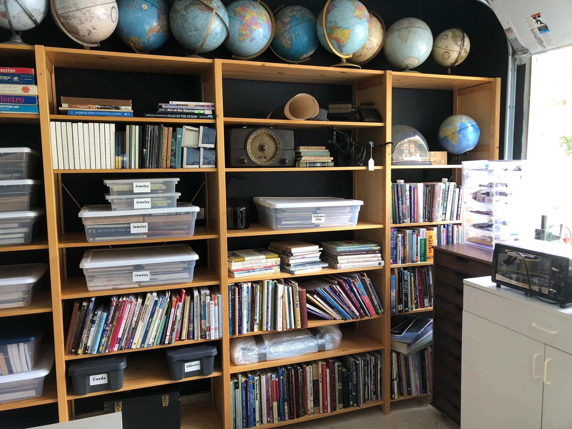Wooden bookshelves filled with books, globes on top shelf, storage bins, and a clock.
