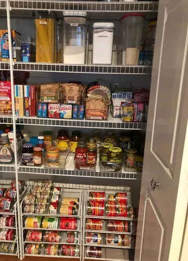 Pantry with wire shelving, organized food items: pasta, canned goods, jars, and clear containers with dry goods.