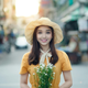 Woman wearing a yellow dress and straw hat, holding flowers, smiling, with a street background.