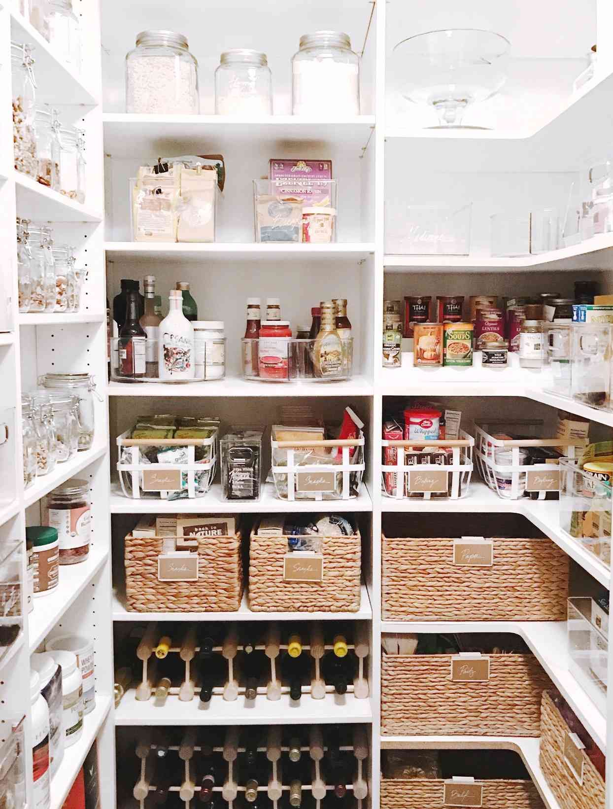 White pantry with organized shelves of food, glass jars, wicker baskets, and a wine rack.