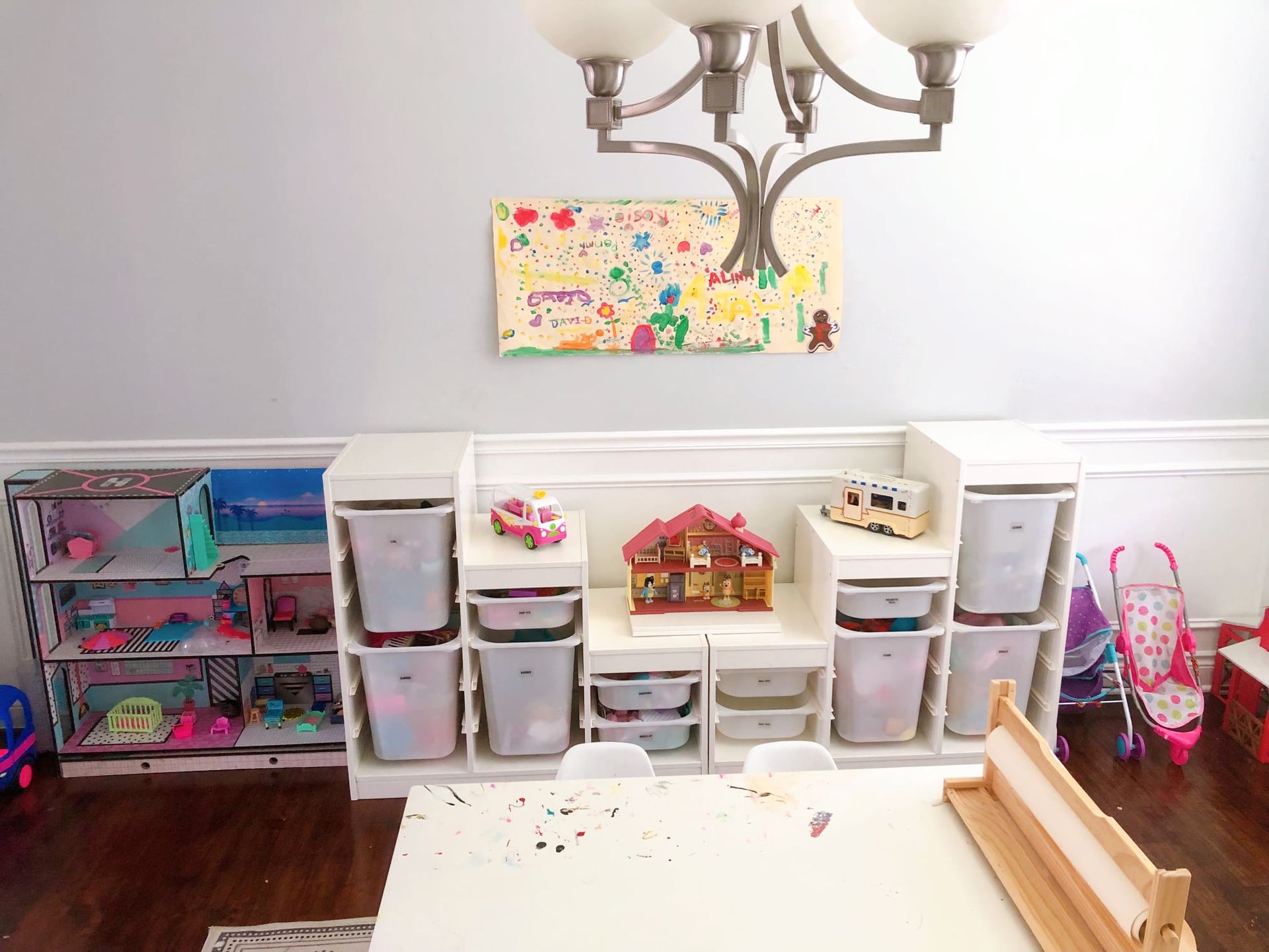 A playroom with toy storage, a dollhouse, and a child's artwork on a light-blue wall.
