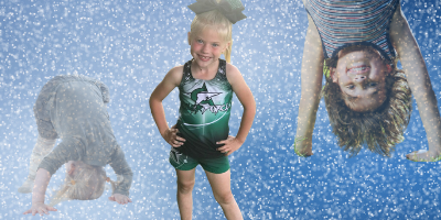 Three young cheerleaders in front of blue, glittery background. One standing, smiling; two doing cartwheels.