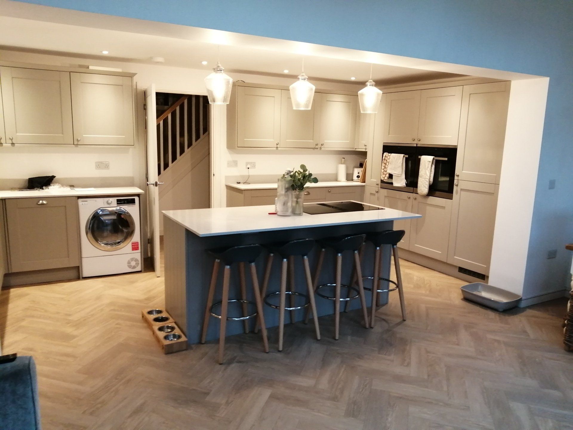 A kitchen with a large island , stools , a washer and dryer , and a staircase.