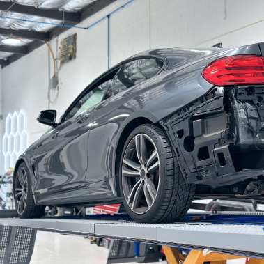 Dark gray BMW coupe on a lift in a repair shop, rear bumper removed. | Ma's Auto Body