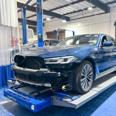 Blue car in auto repair shop; front bumper removed, on a lift. | Ma's Auto Body