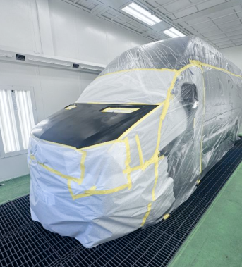 Van in a paint booth, covered in plastic and tape, ready for painting. | Ma's Auto Body
