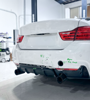 White BMW car's rear bumper, with markings, in a workshop. Black exhaust pipes and diffuser. | Ma's Auto Body