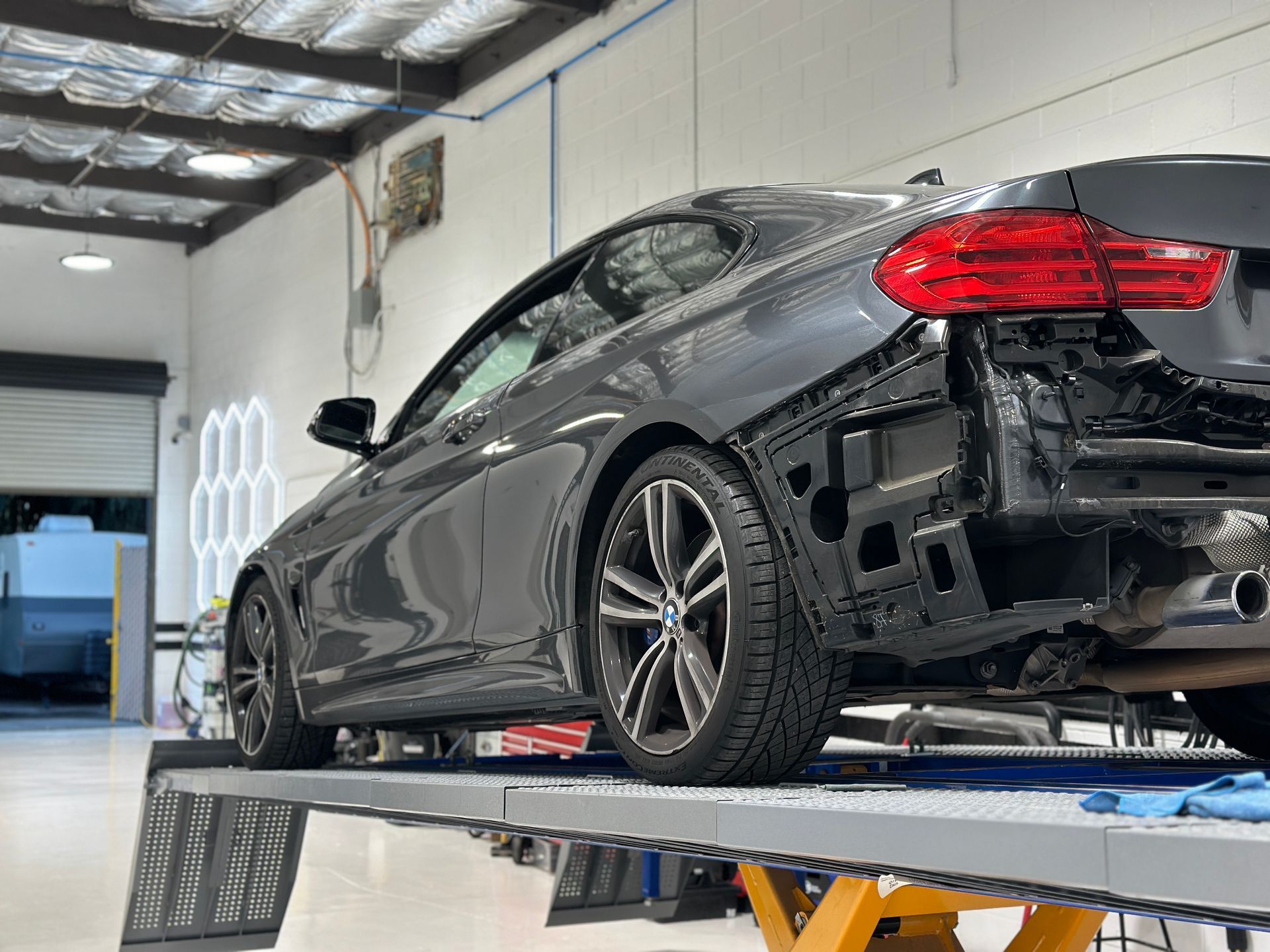 Dark gray BMW coupe on a lift in a workshop, rear quarter view. | Ma's Auto Body