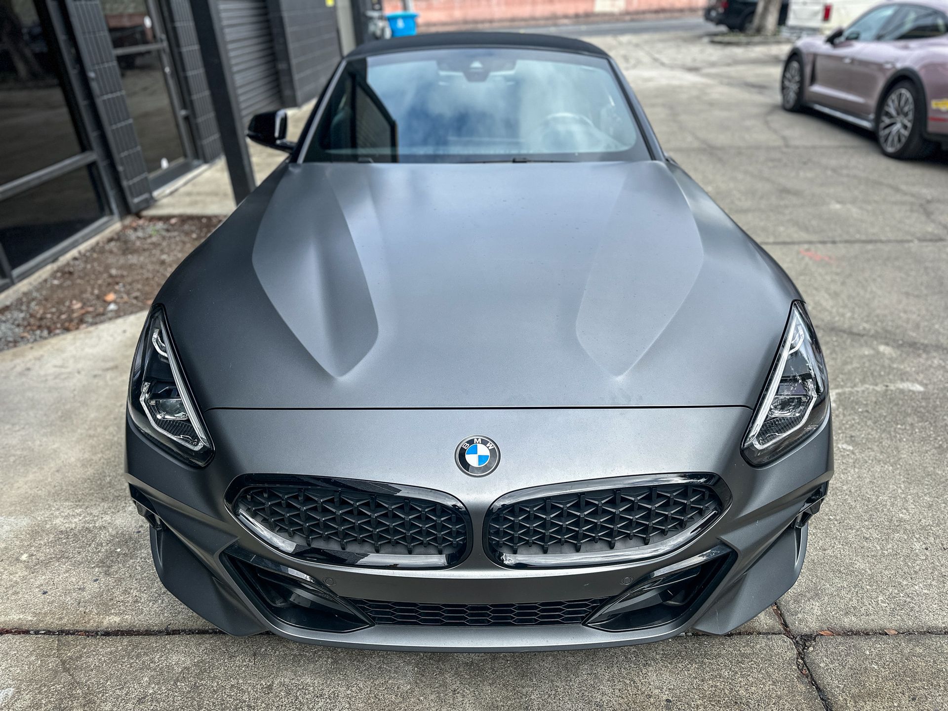 Gray BMW Z4 convertible, front view. Black grille, headlights, and front bumper. Parked on a street. | Ma's Auto Body