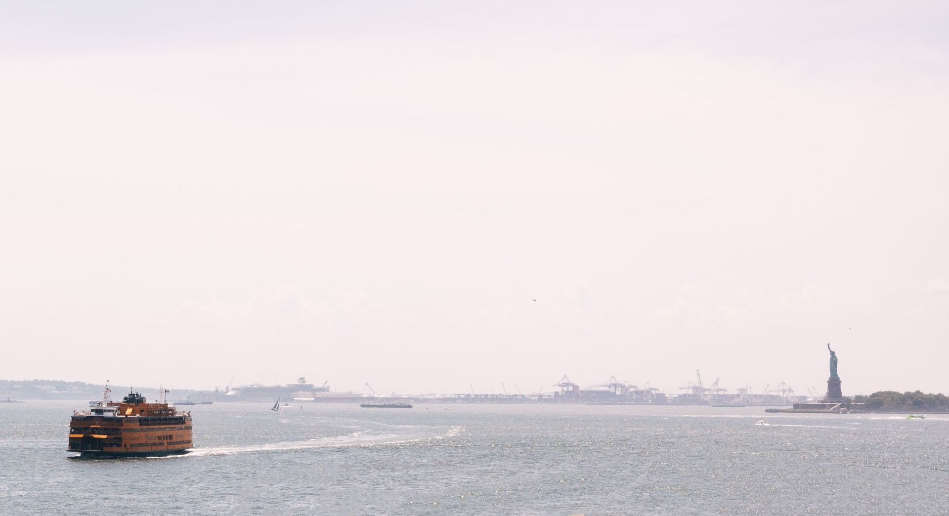 A ferry is going through a body of water with the statue of liberty in the background.