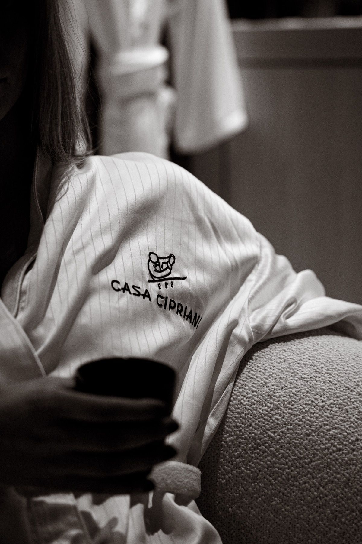 A woman in a robe is sitting on a couch holding a cup of coffee.