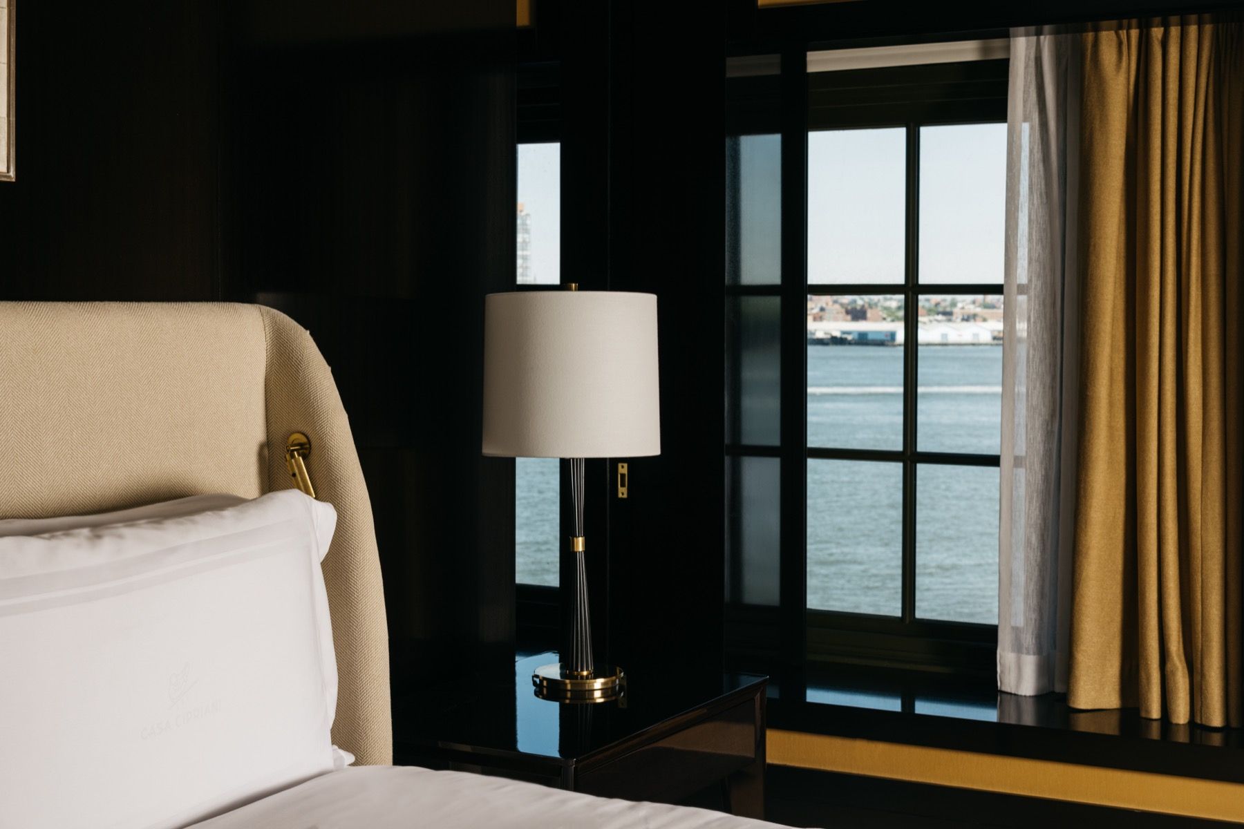 A hotel room with a bed , lamp , and window overlooking the water.