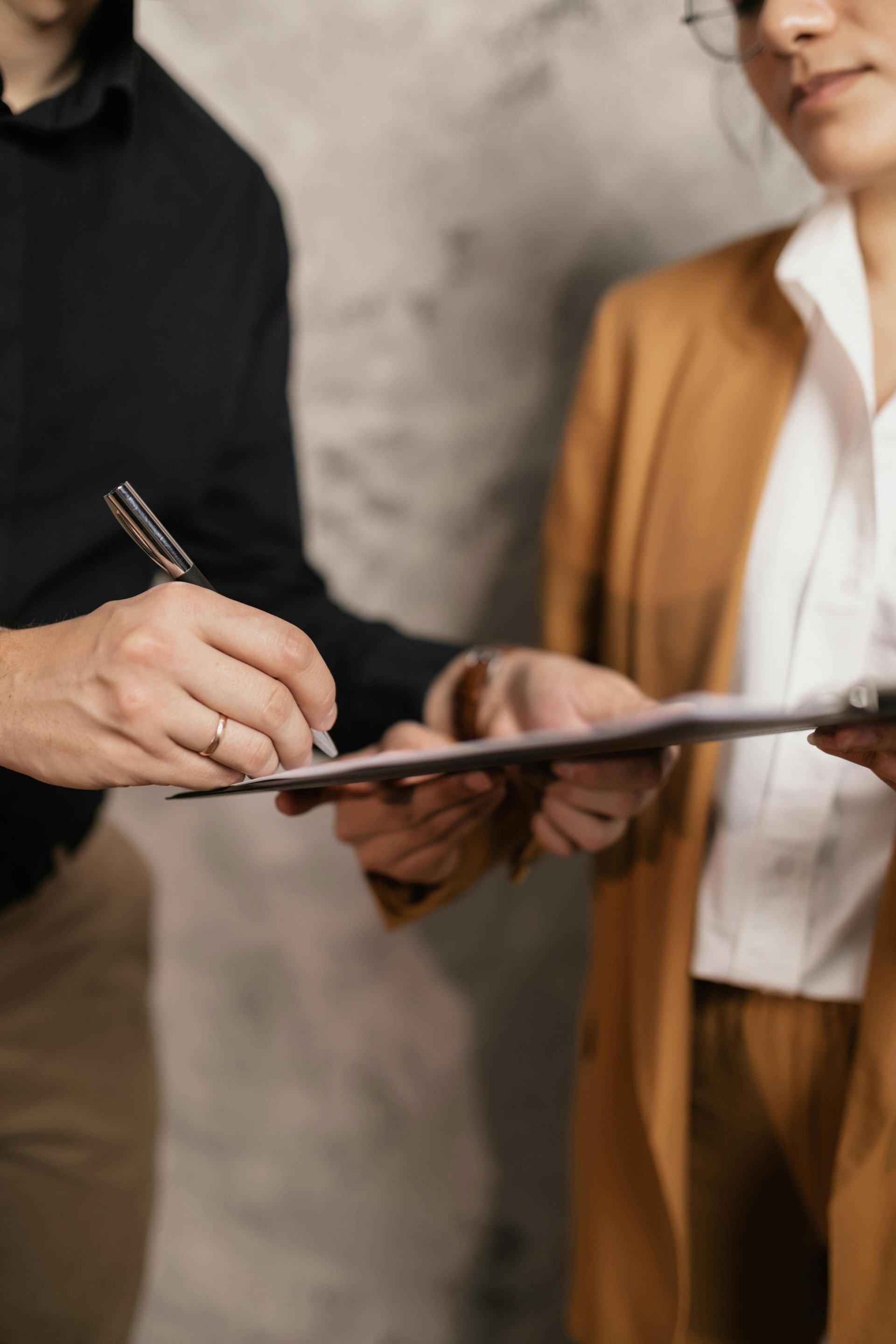 A man is writing on a clipboard while a woman looks on.