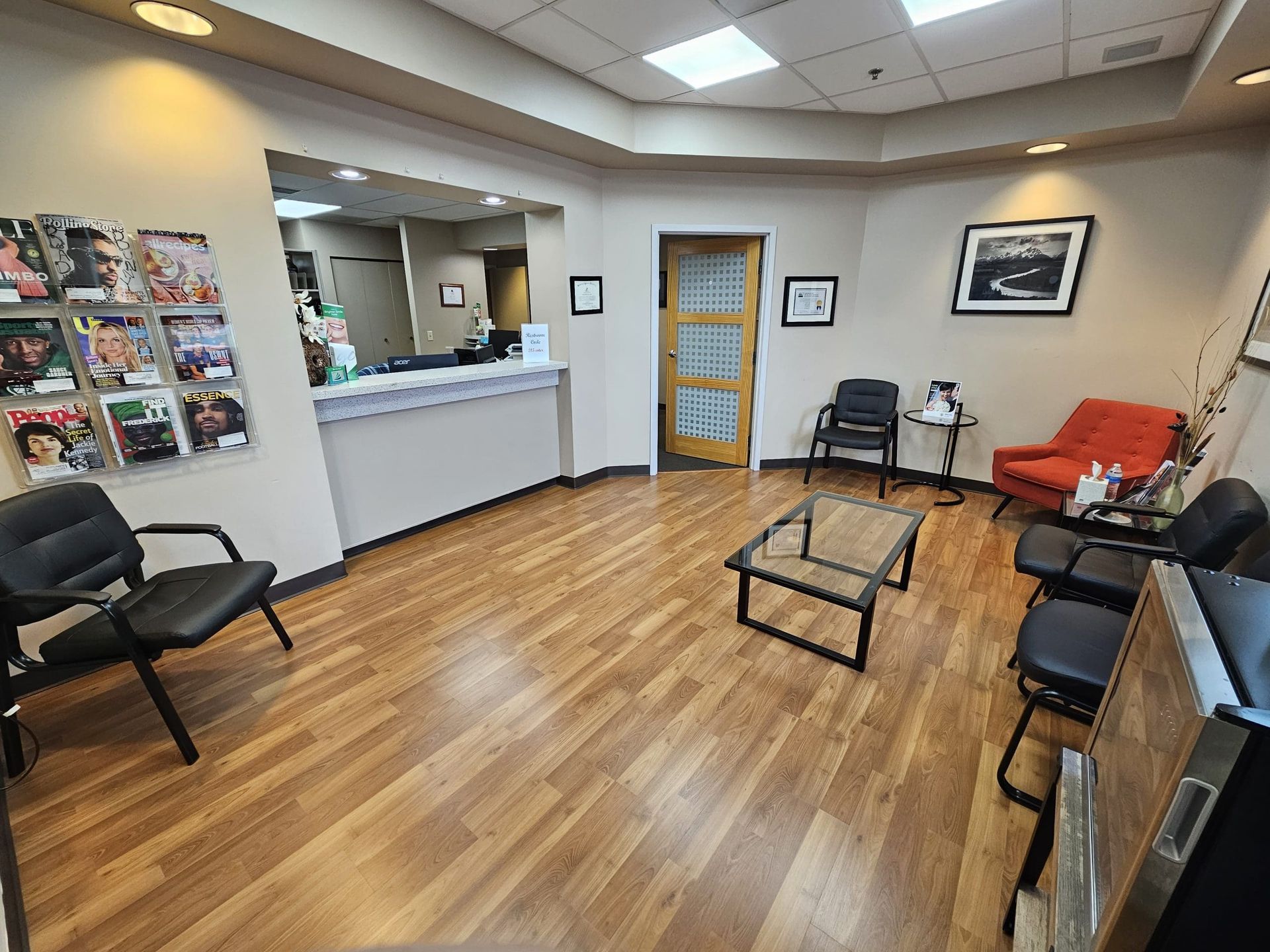 A waiting room with wooden floors , chairs , a coffee table and a counter.