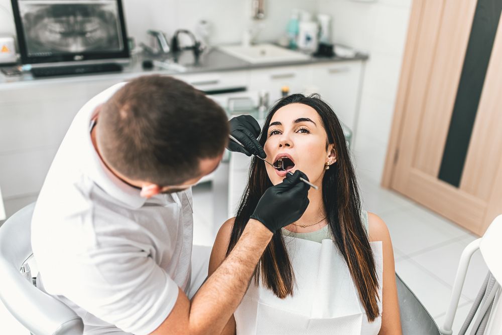 A dentist is examining a woman 's teeth in a dental office.